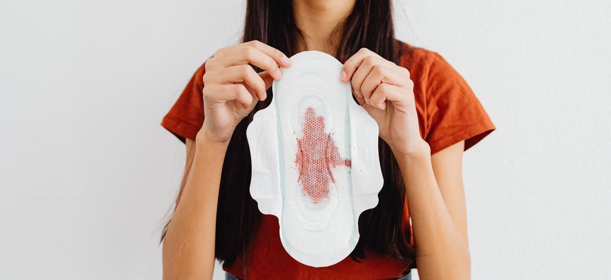 Young woman holding a sanitary pad demonstrating menstrual health awareness indoors.