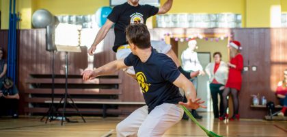 Energetic capoeira performance indoors with audience during daytime.