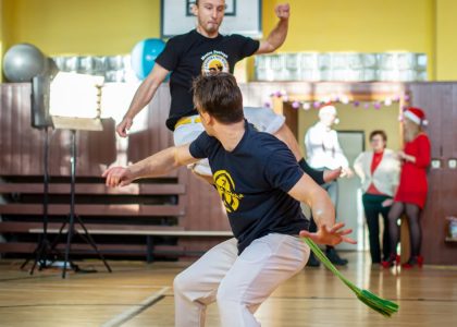 Energetic capoeira performance indoors with audience during daytime.